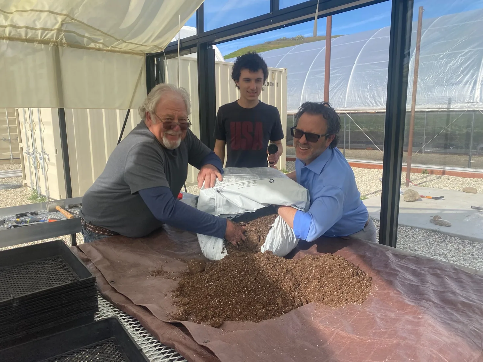 Ben and a farm family mixing propagation media together in a greenhouse