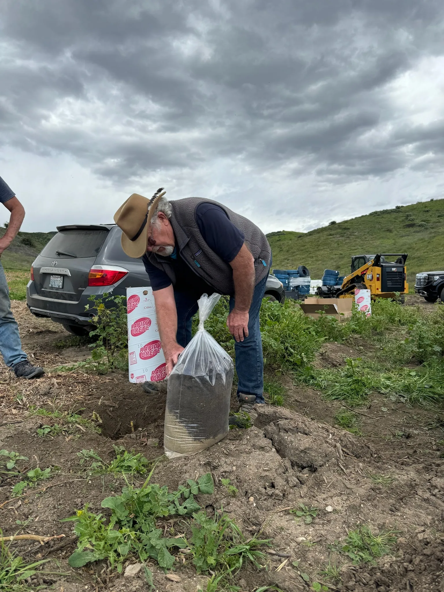 Ben inspecting soil and a planting hole under storm clouds